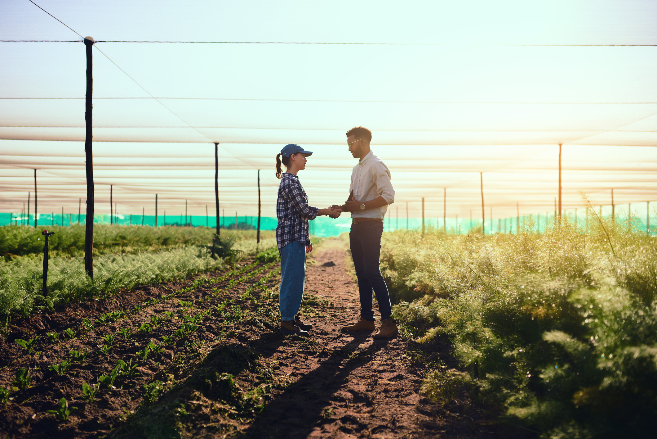 Full length shot of two young farmers shaking hands while working on their farm
